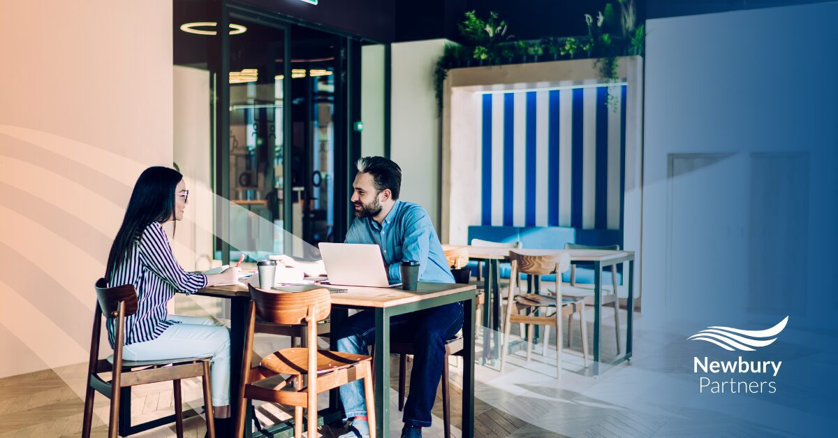 Two staffing professionals discuss commissions maturity strategy over laptops at a modern office table.